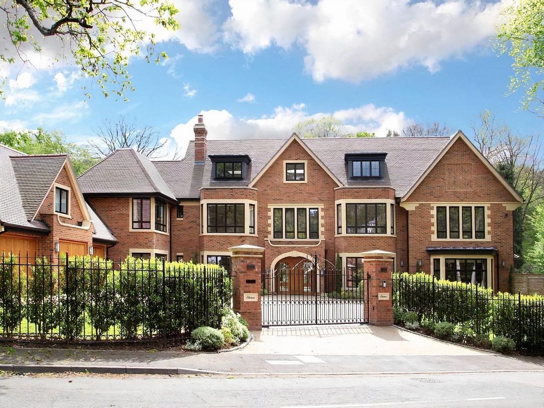 A substantial red-brick country house behind wrought-iron gates on a bright day